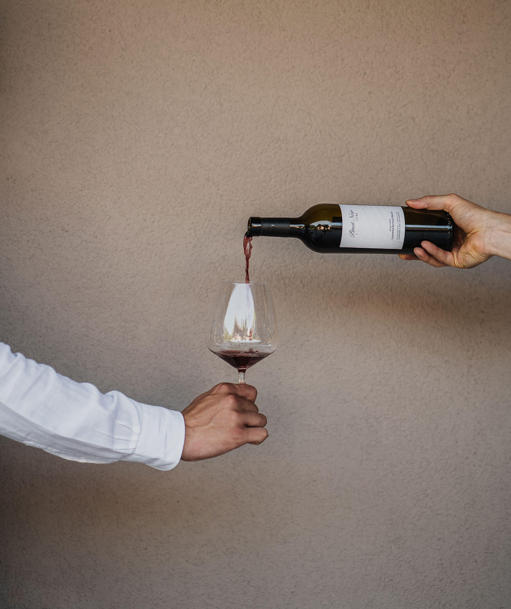 Weinglas mit Rotwein gefüllt in der Hand vor der Wand